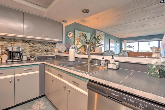 kitchen with sink, gray cabinetry, a textured ceiling, stainless steel dishwasher, and decorative backsplash