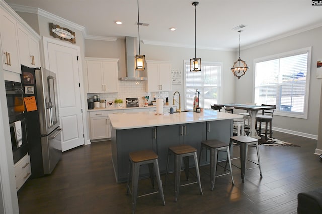 kitchen with a center island with sink, high quality fridge, pendant lighting, wall chimney range hood, and white cabinets