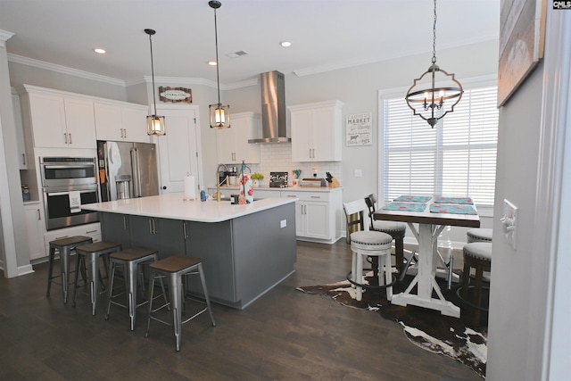 kitchen featuring white cabinets, an island with sink, wall chimney exhaust hood, and appliances with stainless steel finishes