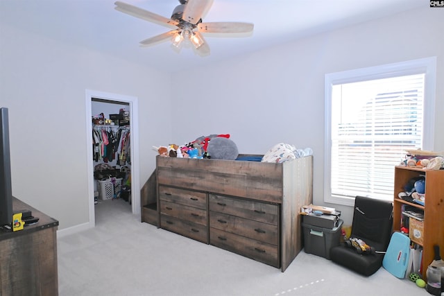 bedroom with a walk in closet, light colored carpet, ceiling fan, and a closet