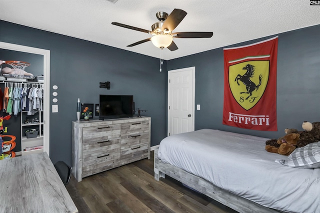 bedroom featuring dark wood-type flooring, a spacious closet, a textured ceiling, a closet, and ceiling fan