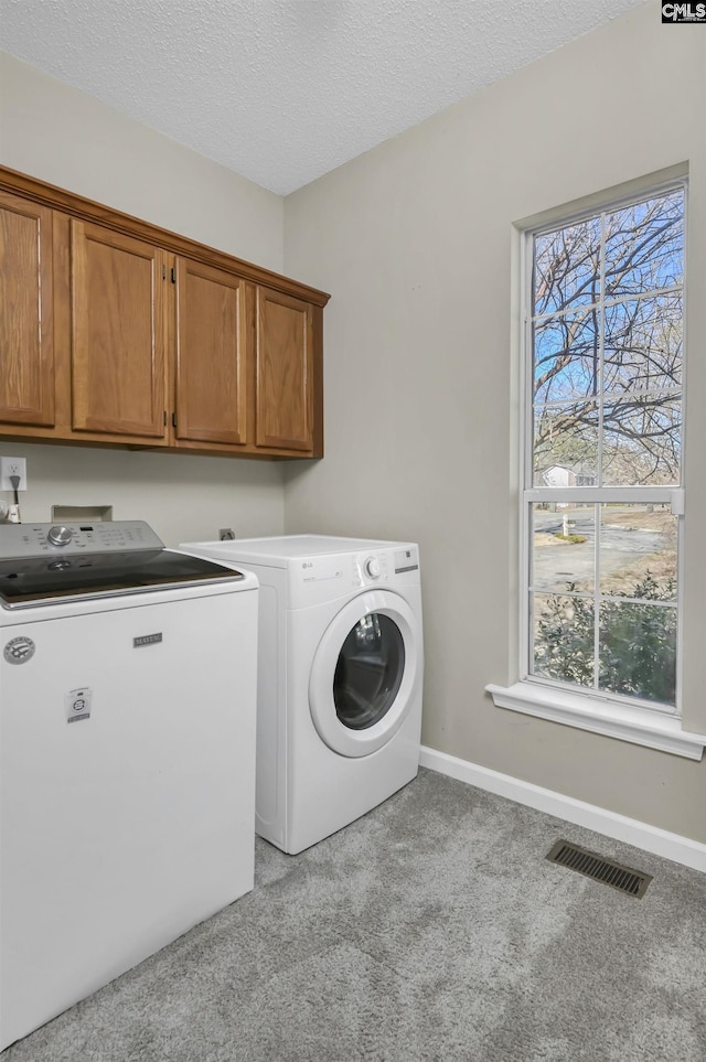 washroom with cabinets, washer and dryer, light carpet, and a textured ceiling