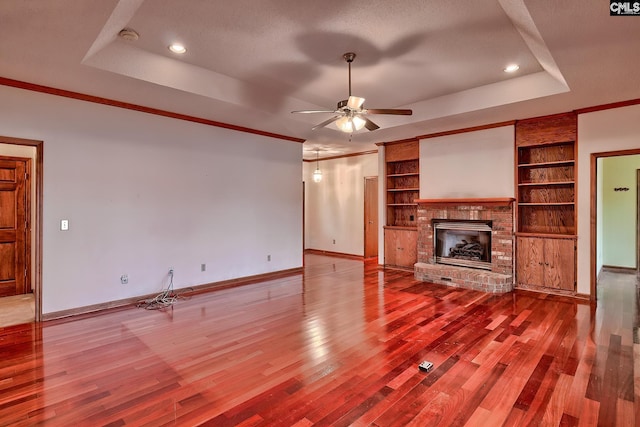 unfurnished living room featuring built in features, a raised ceiling, light hardwood / wood-style floors, and a brick fireplace