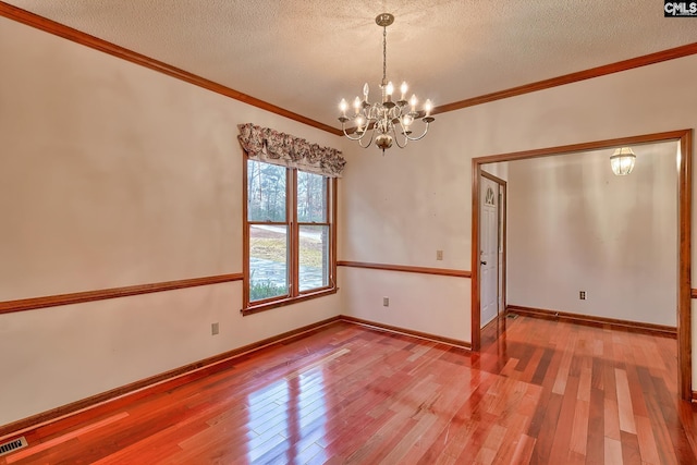 empty room with crown molding, hardwood / wood-style flooring, a chandelier, and a textured ceiling