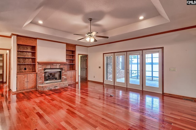 unfurnished living room featuring hardwood / wood-style flooring, ornamental molding, a fireplace, and a raised ceiling