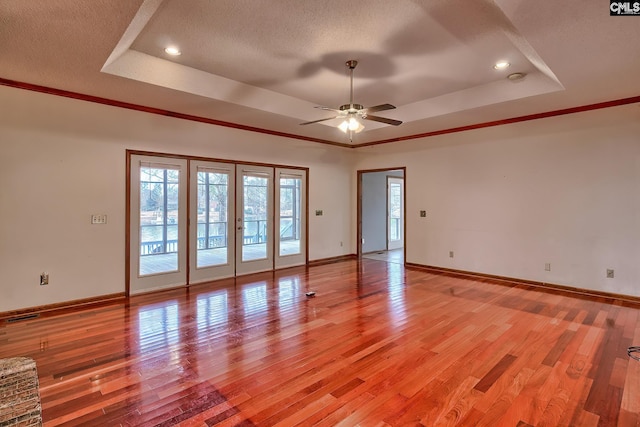 unfurnished room with crown molding, a textured ceiling, light wood-type flooring, and a tray ceiling