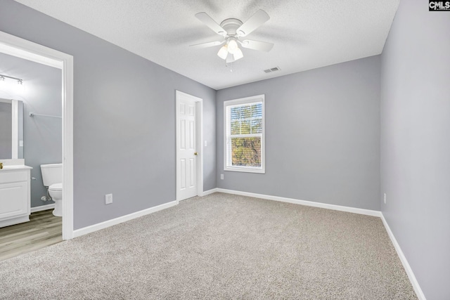 unfurnished bedroom featuring light carpet, a textured ceiling, and ensuite bath