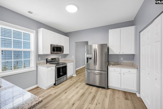 kitchen with light stone counters, light wood-type flooring, white cabinets, and appliances with stainless steel finishes