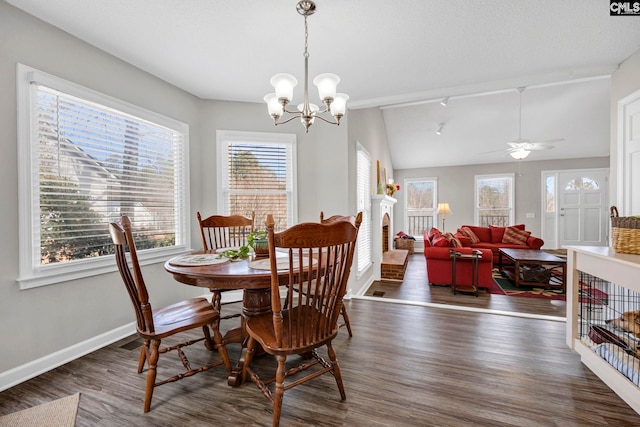 dining space with lofted ceiling, dark wood-type flooring, rail lighting, a textured ceiling, and ceiling fan with notable chandelier