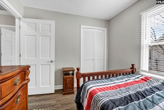 bedroom with multiple windows, dark wood-type flooring, a closet, and a textured ceiling