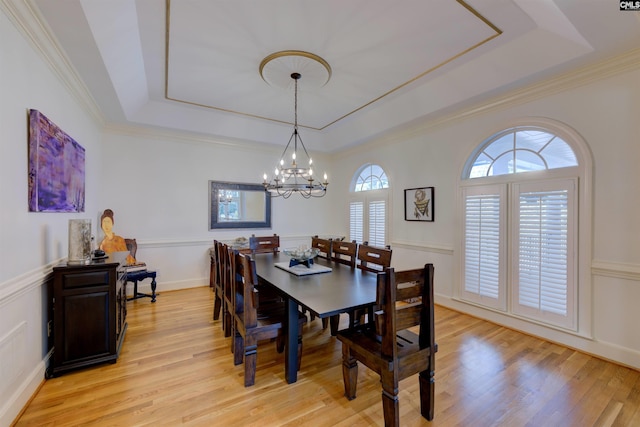 dining area with crown molding, a raised ceiling, light hardwood / wood-style floors, and a notable chandelier