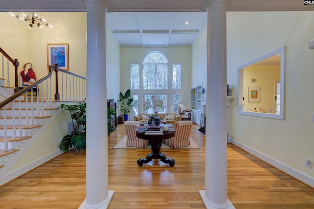 foyer with a towering ceiling, decorative columns, beamed ceiling, coffered ceiling, and light hardwood / wood-style flooring