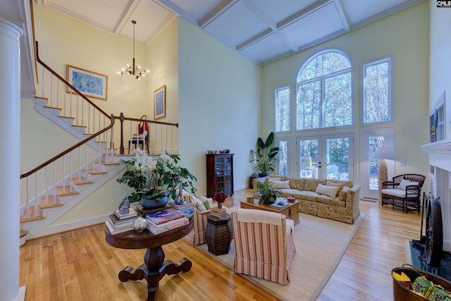 living room with french doors, coffered ceiling, light hardwood / wood-style flooring, a notable chandelier, and a towering ceiling