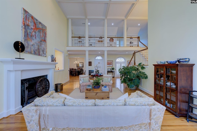 living room with an inviting chandelier, a fireplace, light hardwood / wood-style floors, and a high ceiling