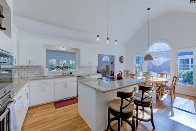 kitchen with decorative light fixtures, sink, oven, white cabinets, and a center island