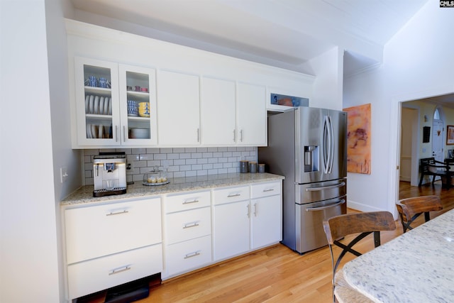 kitchen with stainless steel fridge with ice dispenser, light wood-type flooring, light stone countertops, decorative backsplash, and white cabinets