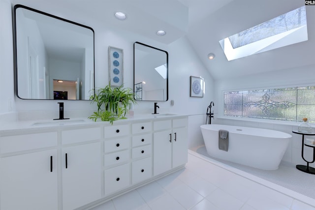 bathroom featuring tile patterned floors, vanity, vaulted ceiling with skylight, and a bathtub