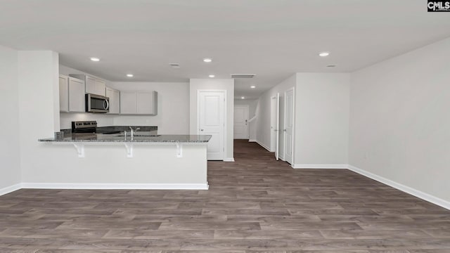 kitchen featuring a breakfast bar, kitchen peninsula, stainless steel appliances, light stone countertops, and dark wood-type flooring