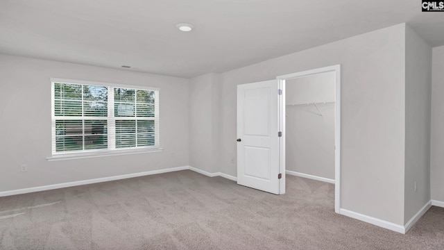 unfurnished bedroom featuring a walk in closet, light carpet, and a closet