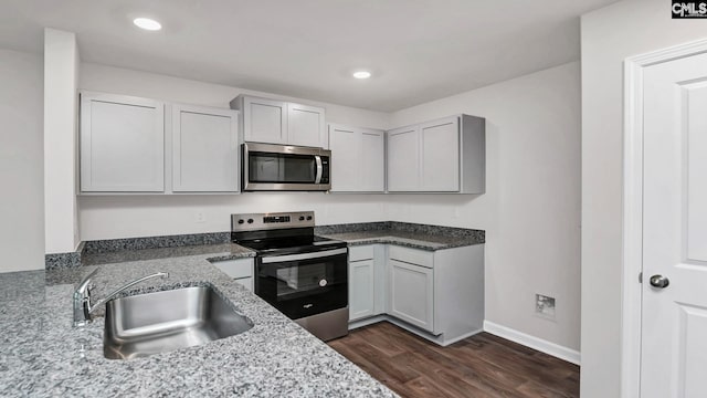 kitchen with sink, dark wood-type flooring, appliances with stainless steel finishes, gray cabinetry, and light stone countertops