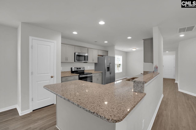 kitchen with light wood-type flooring, gray cabinets, kitchen peninsula, stainless steel appliances, and light stone countertops