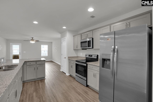 kitchen with gray cabinets, appliances with stainless steel finishes, sink, light stone counters, and light hardwood / wood-style floors