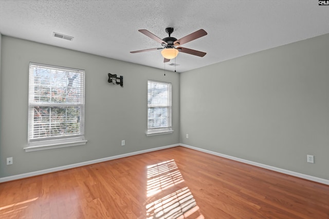 unfurnished room featuring baseboards, visible vents, ceiling fan, wood finished floors, and a textured ceiling