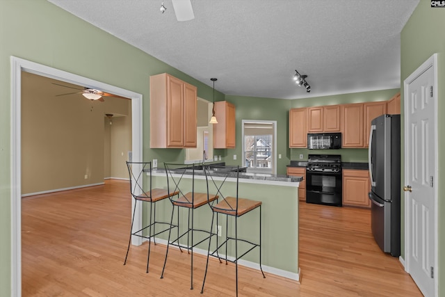 kitchen featuring black appliances, a breakfast bar area, hanging light fixtures, ceiling fan, and kitchen peninsula