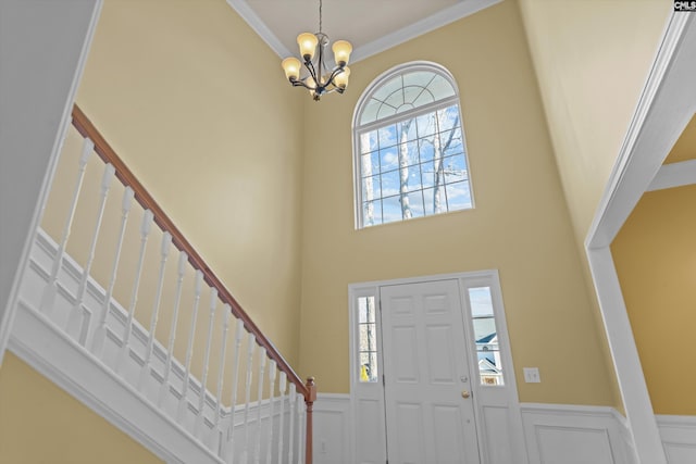 foyer entrance with an inviting chandelier, a towering ceiling, and ornamental molding