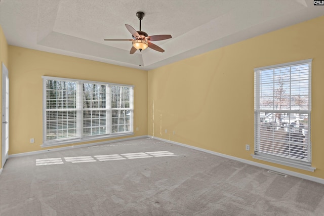 unfurnished room featuring ceiling fan, light colored carpet, a raised ceiling, and a textured ceiling