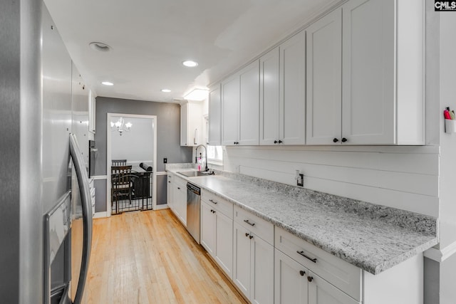 kitchen with stainless steel appliances, white cabinetry, light stone countertops, and sink