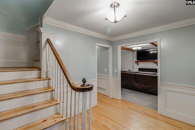 stairway with wood-type flooring, crown molding, a fireplace, and a textured ceiling