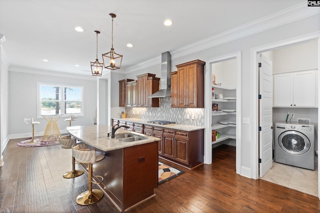 kitchen with sink, a center island with sink, a kitchen bar, washer / clothes dryer, and wall chimney exhaust hood