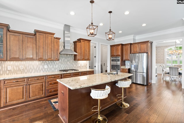 kitchen with a breakfast bar area, hanging light fixtures, a center island with sink, stainless steel appliances, and wall chimney range hood