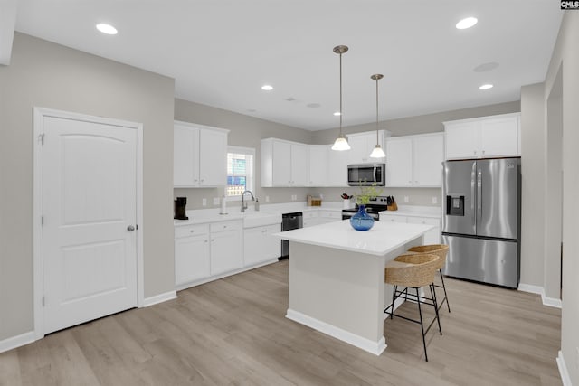 kitchen featuring stainless steel appliances, a center island, light hardwood / wood-style floors, white cabinets, and decorative light fixtures