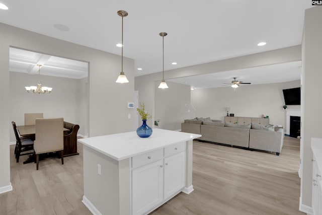 kitchen with white cabinetry, hanging light fixtures, light hardwood / wood-style flooring, a kitchen island, and ceiling fan with notable chandelier