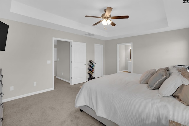 bedroom with light carpet, ensuite bath, a raised ceiling, and ceiling fan