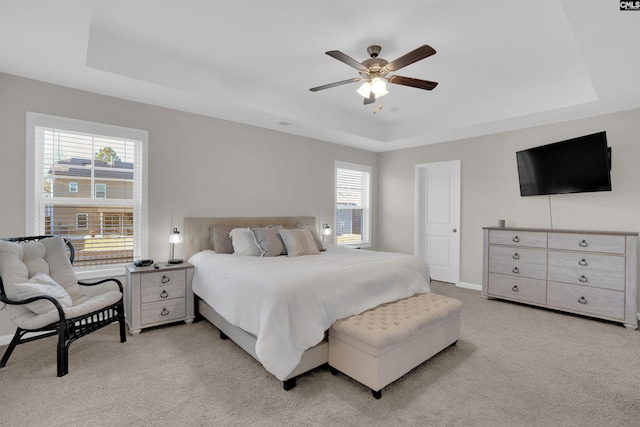 bedroom with light carpet, ceiling fan, and a tray ceiling