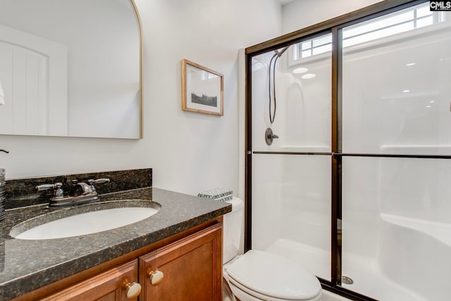 bathroom featuring vanity, a shower with shower door, and toilet