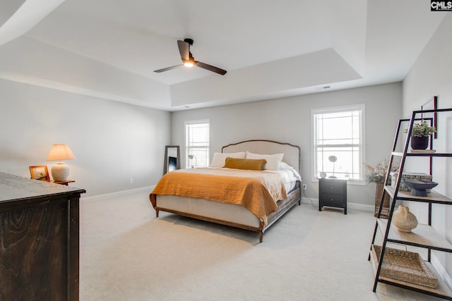 bedroom with light colored carpet, ceiling fan, and a tray ceiling