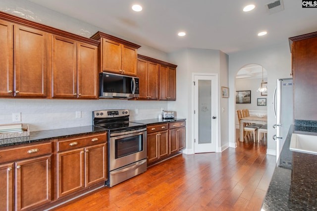 kitchen with dark wood-type flooring, tasteful backsplash, hanging light fixtures, dark stone counters, and stainless steel appliances