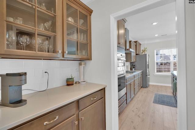 kitchen with crown molding, stainless steel appliances, light wood-type flooring, and backsplash