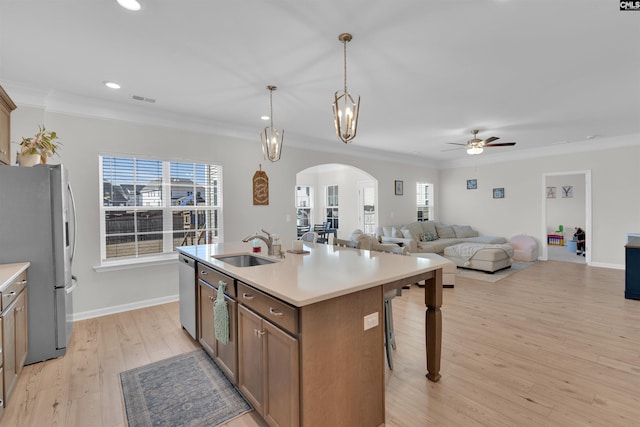 kitchen with sink, hanging light fixtures, light hardwood / wood-style flooring, appliances with stainless steel finishes, and an island with sink