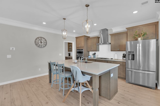 kitchen featuring sink, hanging light fixtures, a center island with sink, appliances with stainless steel finishes, and wall chimney range hood