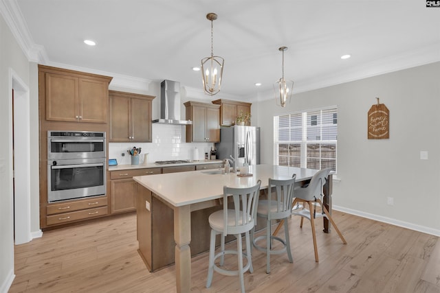 kitchen with sink, appliances with stainless steel finishes, hanging light fixtures, a center island with sink, and wall chimney exhaust hood