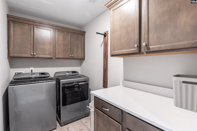 clothes washing area with cabinets, washer and dryer, and light hardwood / wood-style floors