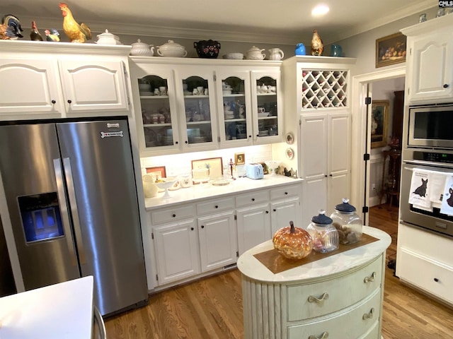 kitchen with white cabinetry, ornamental molding, appliances with stainless steel finishes, a kitchen island, and hardwood / wood-style floors