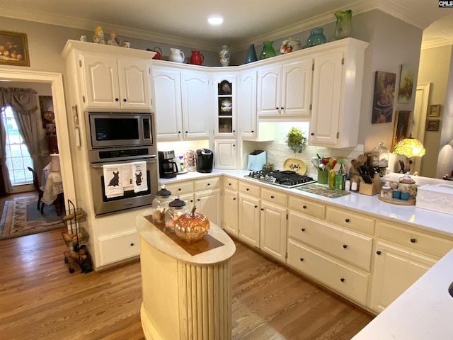 kitchen featuring ornamental molding, appliances with stainless steel finishes, light hardwood / wood-style floors, and backsplash