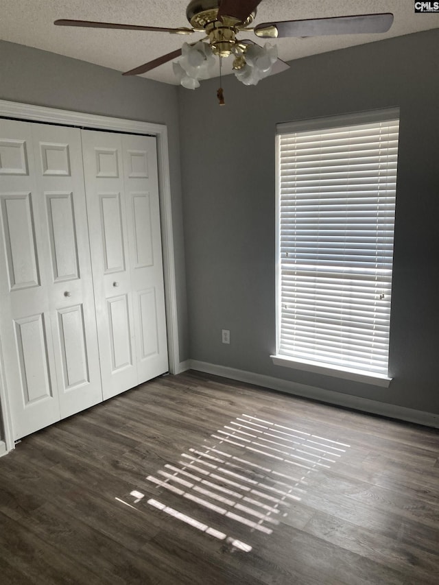 unfurnished bedroom featuring dark wood-type flooring, a textured ceiling, ceiling fan, and a closet