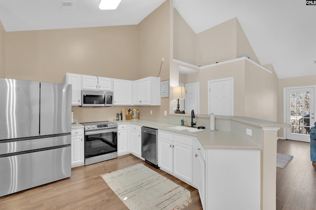 kitchen featuring appliances with stainless steel finishes, high vaulted ceiling, white cabinetry, sink, and kitchen peninsula